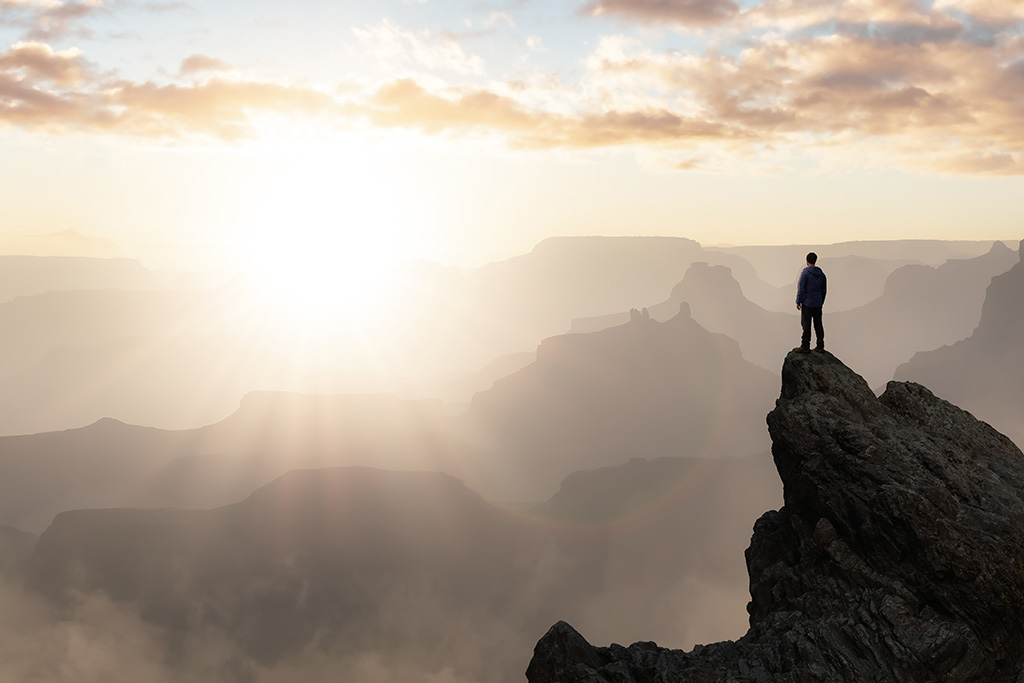 Man looking out from the top of the mountain to the sky considering heaven
