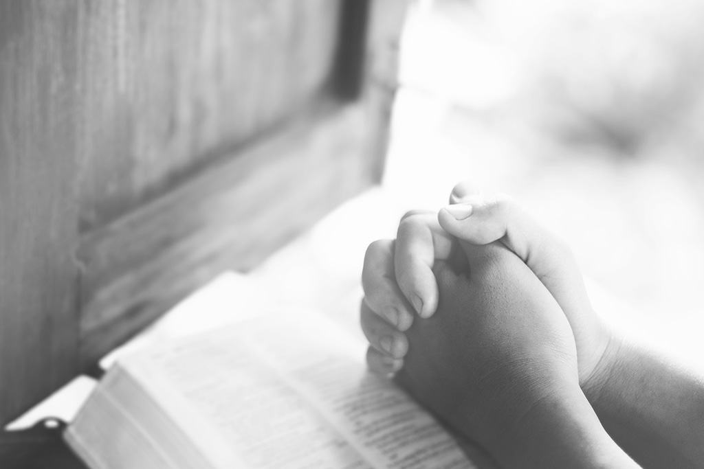 praying hands on top of a Bible